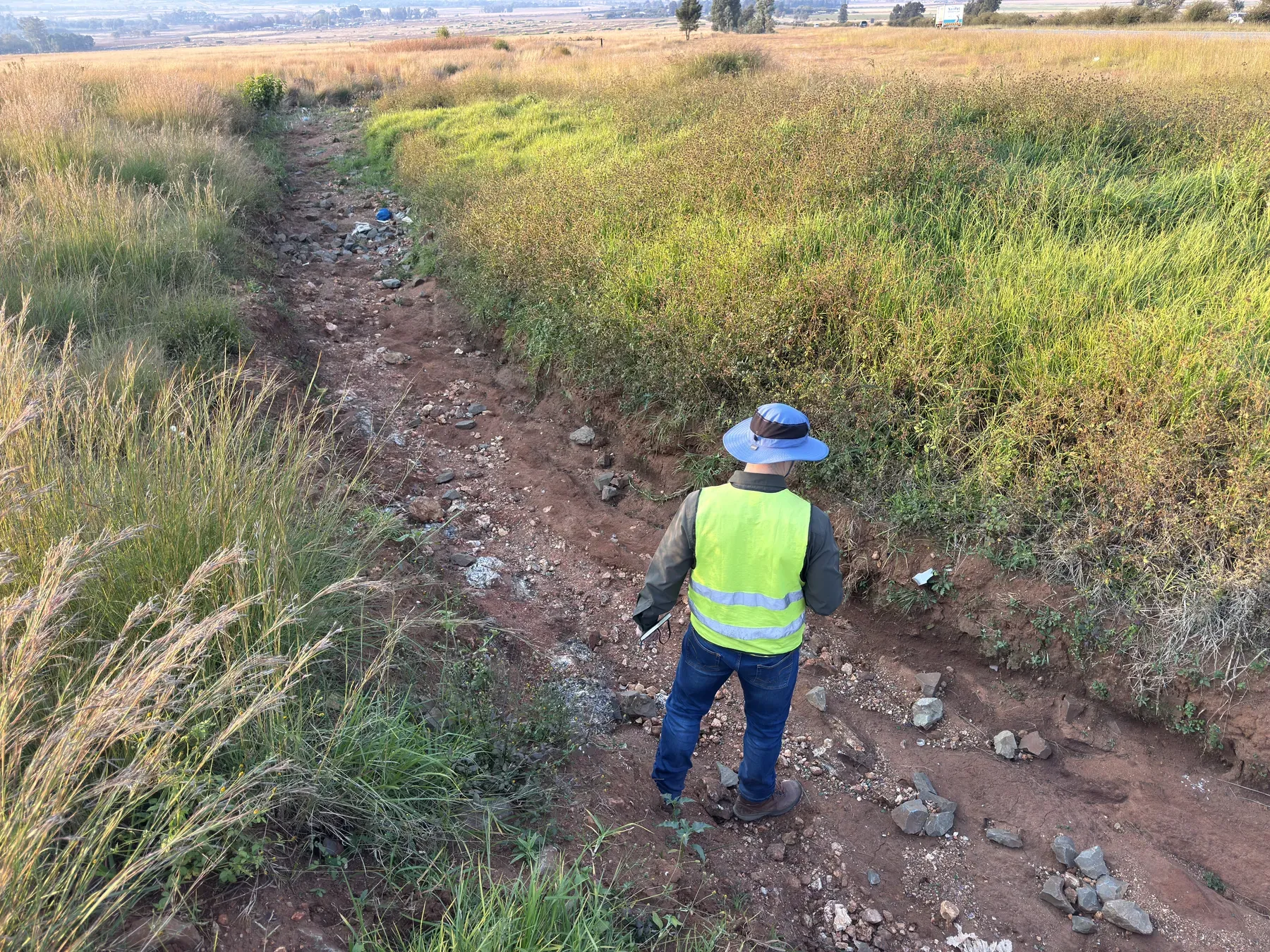 Engineer inspecting a scoured drainage channel where displaced riprap has failed to stop erosion.