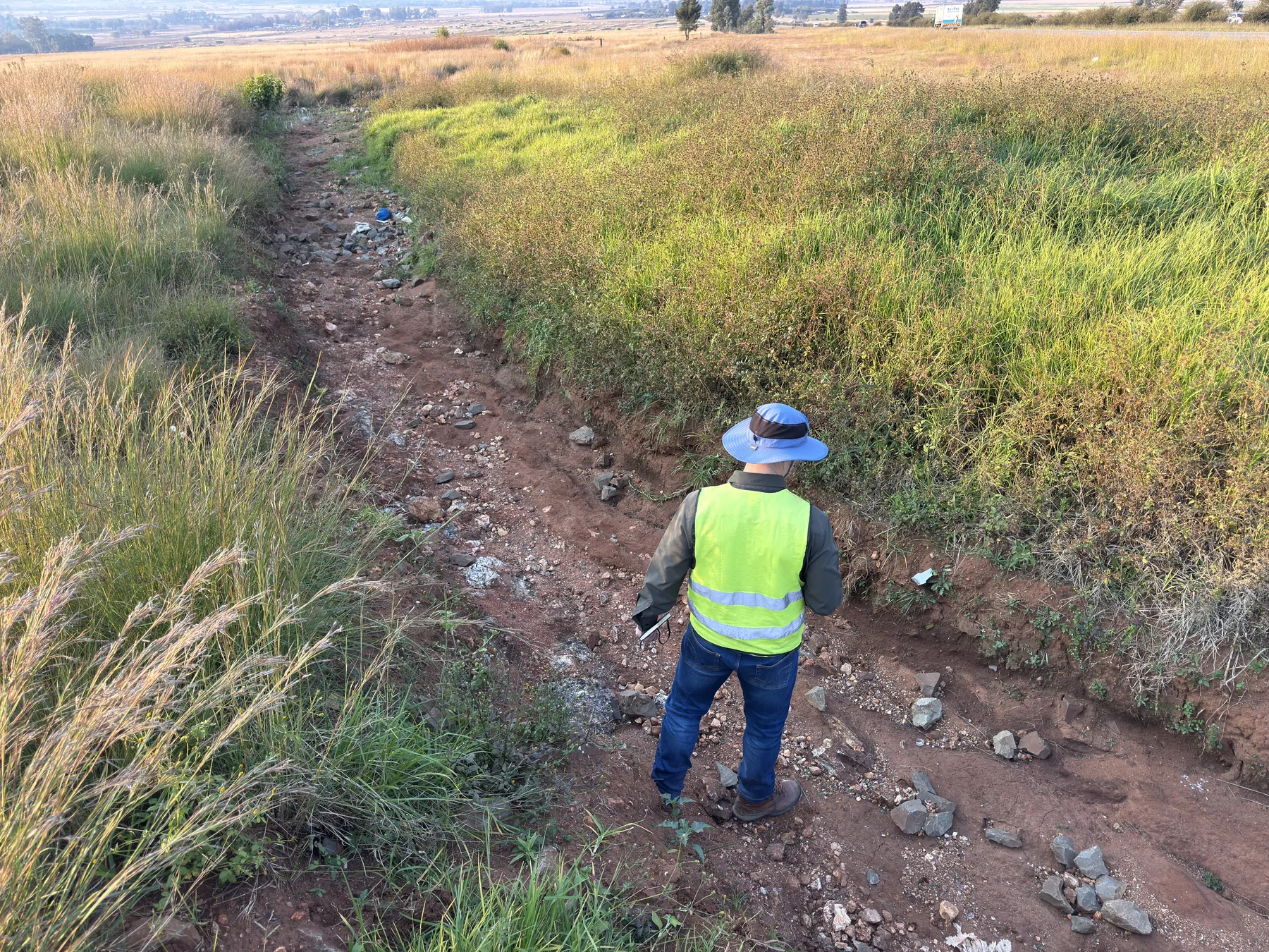 Engineer inspecting a scoured drainage channel where displaced riprap has failed to stop erosion.