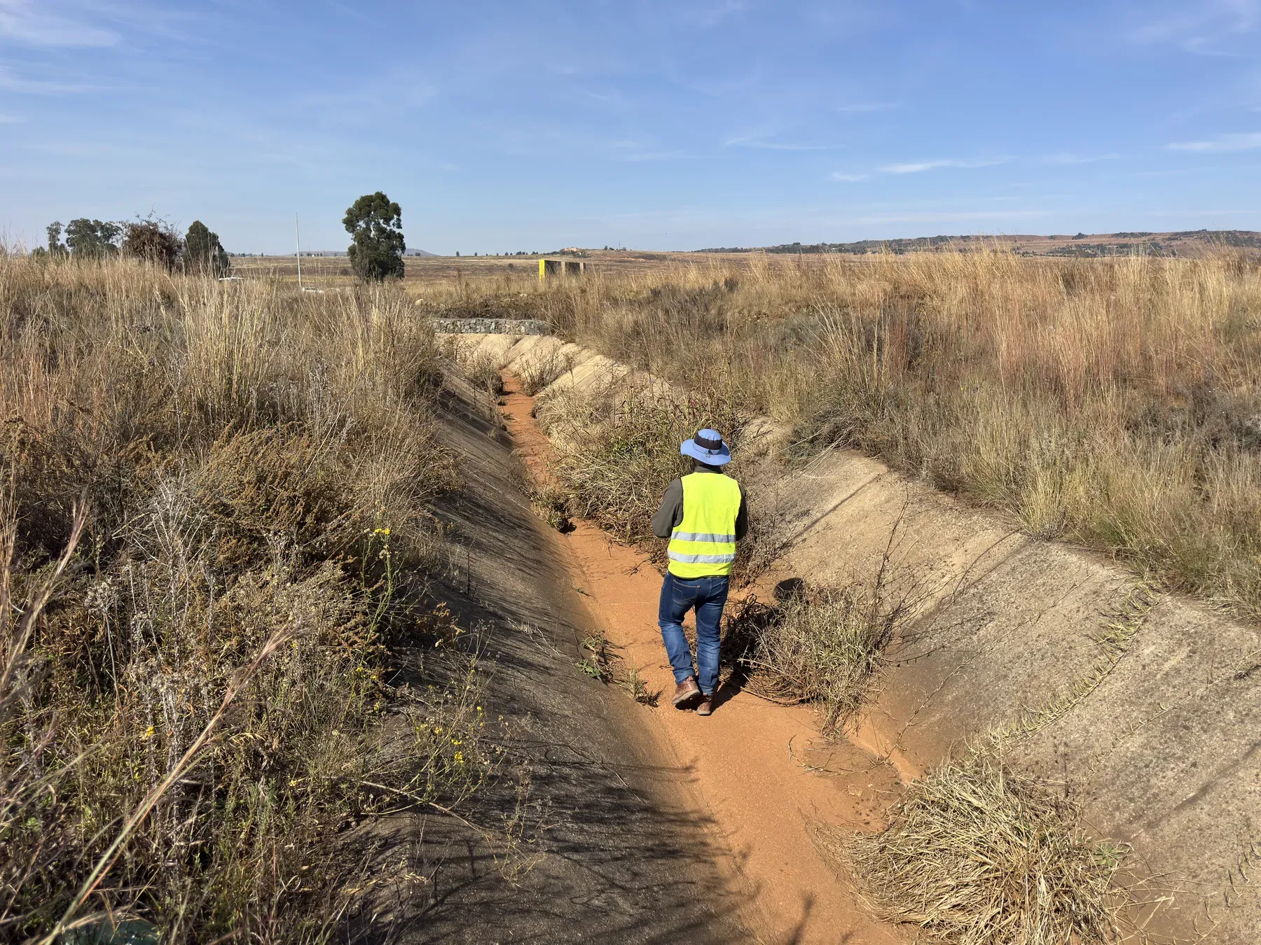 Engineer walking down a concrete-lined stormwater canal partially filled with sediment and vegetation.
