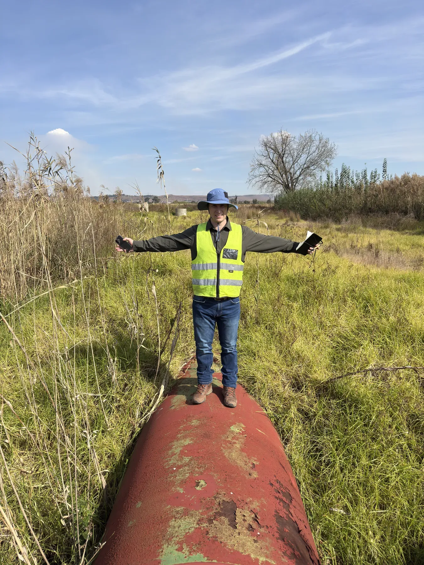 Engineer standing on a large bulk water pipeline running through dense wetland vegetation during an inspection.