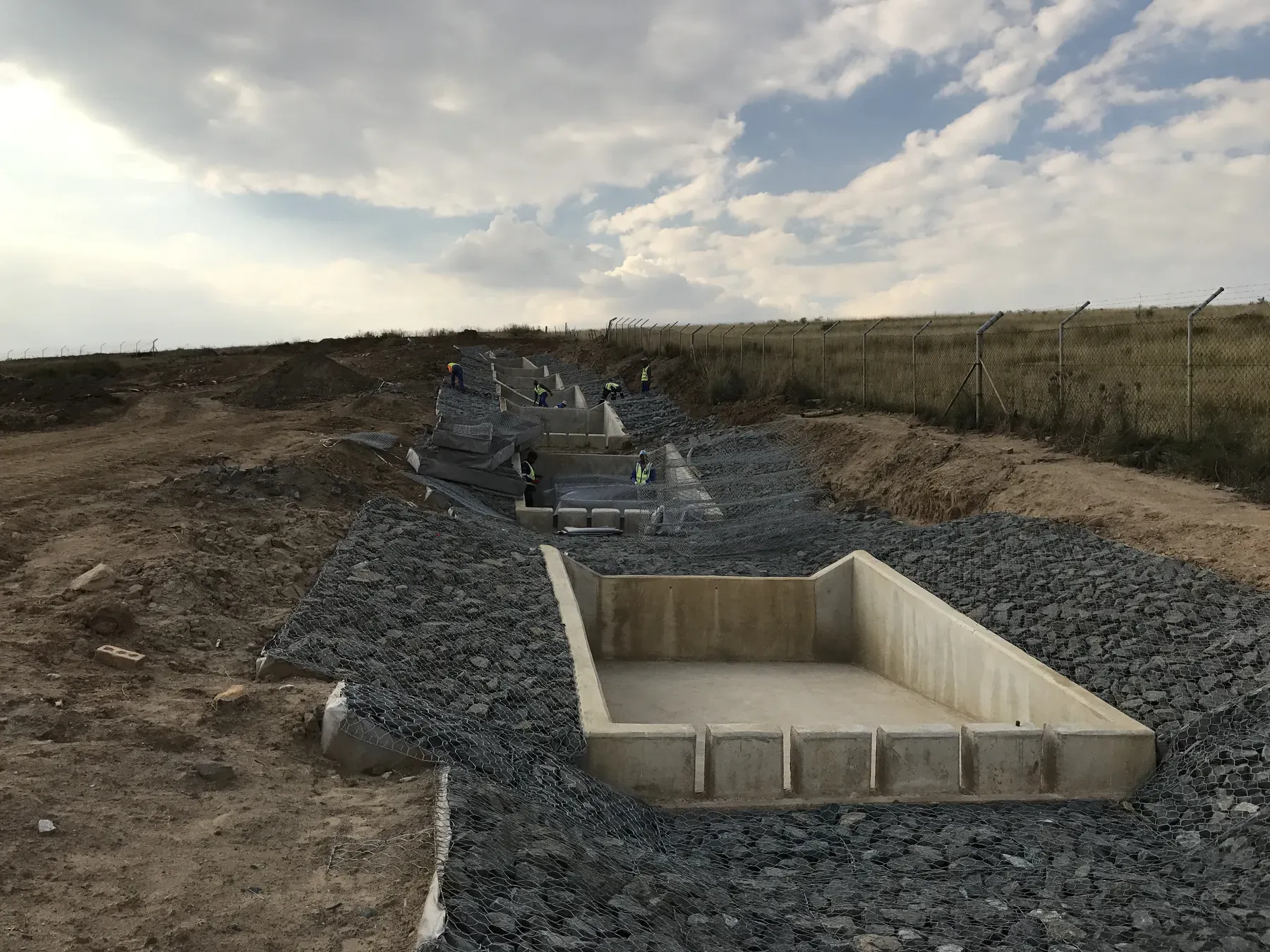 Stepped concrete energy dissipator structures descending a steep grassed slope.